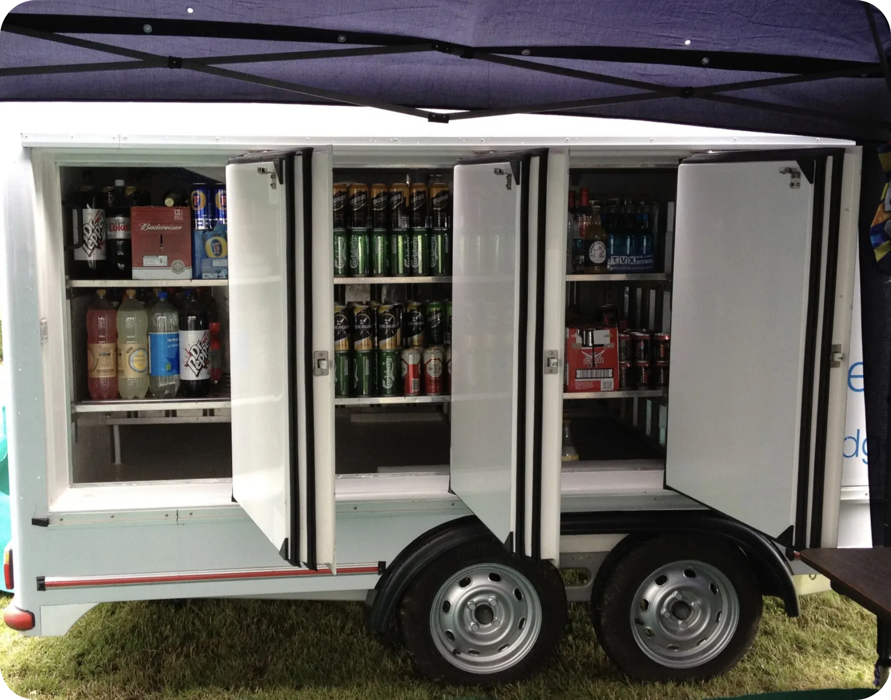 Side view of a mobile refrigeration trailer with doors open, displaying chilled drinks and organised shelving, demonstrating how portable refrigerated storage works for events, catering, and commercial hire.